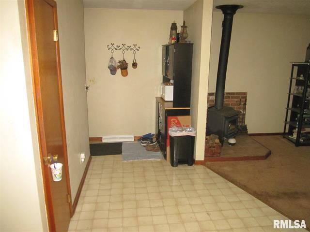A room with a door, tile floor, and a wood-burning stove.
