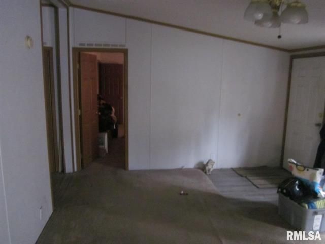 Empty mobile home interior with stained carpet, white walls, and a partially open door