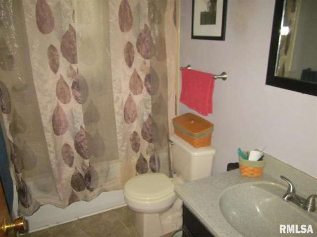 Bathroom with shower curtain, toilet, sink, pink towel, and framed art.