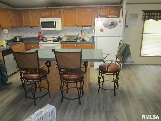 Kitchen with island, cabinets, appliances, and bar stools. Grey flooring