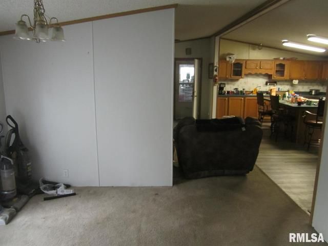 Living area with a partial wall, leading to kitchen with a brown sofa and vacuum