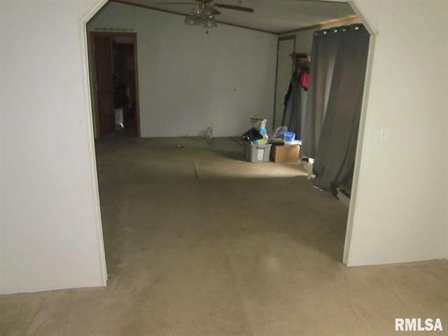 Interior view of a living area with doorway arches, beige carpet, and clutter