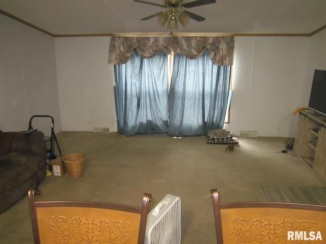 Empty living room with blue curtains, tan carpet, ceiling fan, and brown furniture