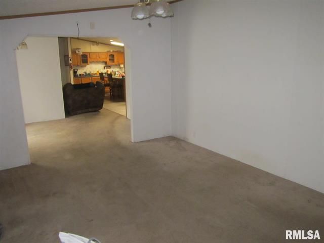Empty living room with tan carpet and doorway to kitchen