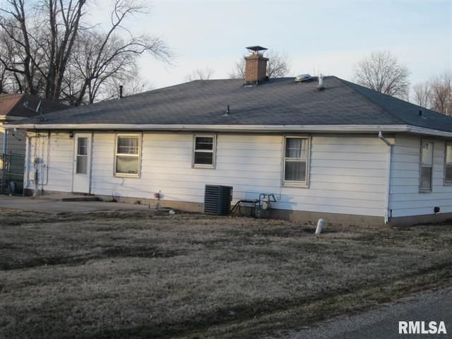 White house with dark roof and chimney, set on a grassy lot, viewed from outdoors.