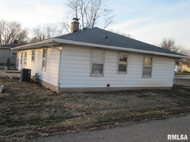 White one-story house with a dark roof and several windows on a grassy lot.