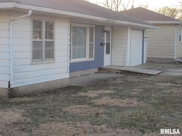 Exterior view of a small, white house with blue accents and a ramp leading to the front door.