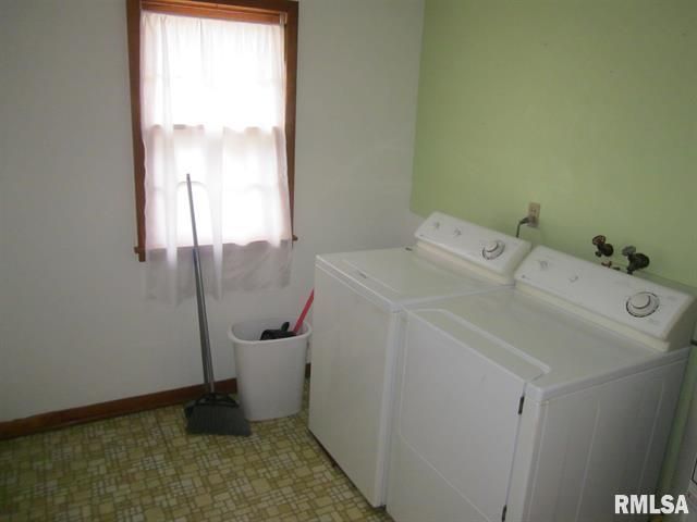 Laundry room with washer, dryer, window with curtain, and broom. Green and white walls, patterned floor.