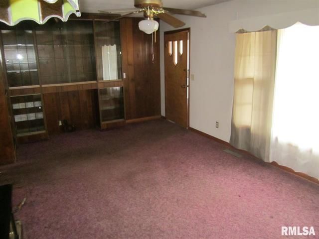Living room with wood paneling, built-in shelving, burgundy carpet, and a closed brown door.