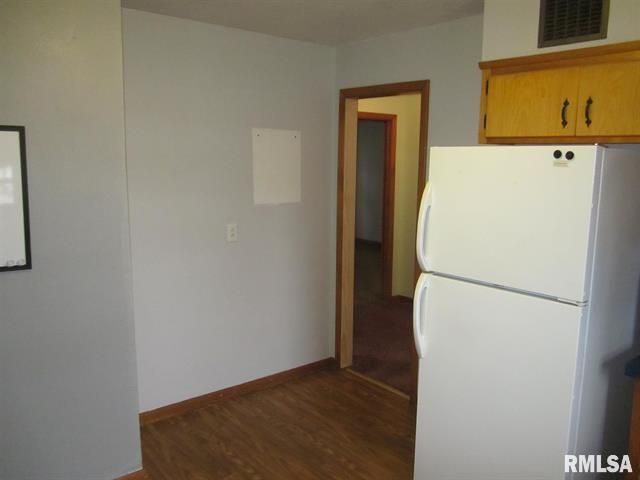 Kitchen interior with gray walls, refrigerator, wooden floor, and doorway to another room.