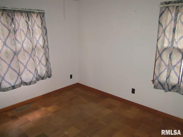 Empty room with wood floor and two windows with patterned curtains.