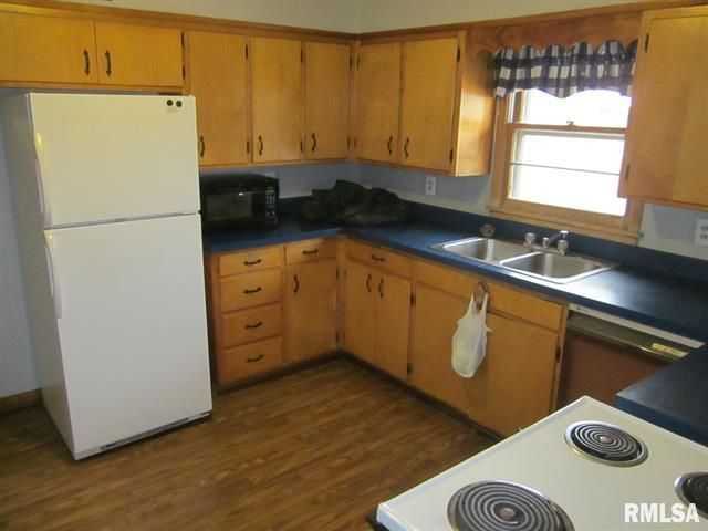 Kitchen with wooden cabinets, blue countertops, white appliances, and a window.