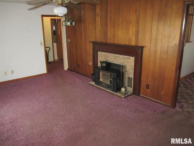 Room with wood paneling, fireplace, purple carpet, and a ceiling fan.