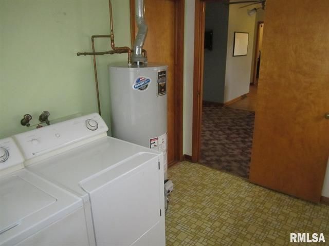 A laundry room with a washing machine, dryer, and water heater. A doorway leads to a hallway.