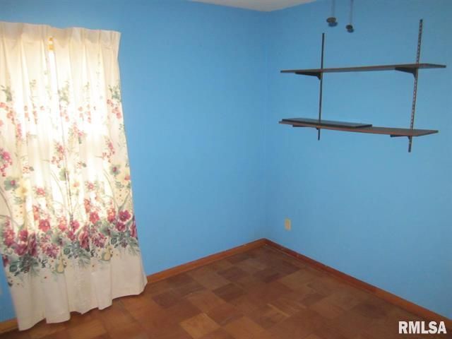 Empty room with blue walls, floral curtains, brown shelves, and a patterned wood floor.