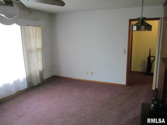 Empty living room with dusty rose carpet, a doorway, and a ceiling fan.