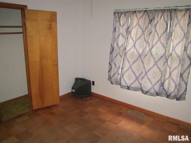 Empty bedroom with wood floor, closet, and patterned curtains. A small heater sits near the window.