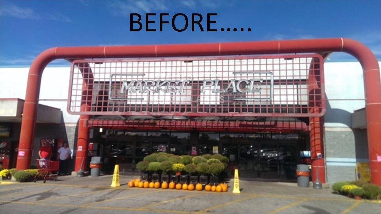 The entrance to a Home Depot store before renovations, featuring a red archway and sign. Green plants and other items are displayed in front.