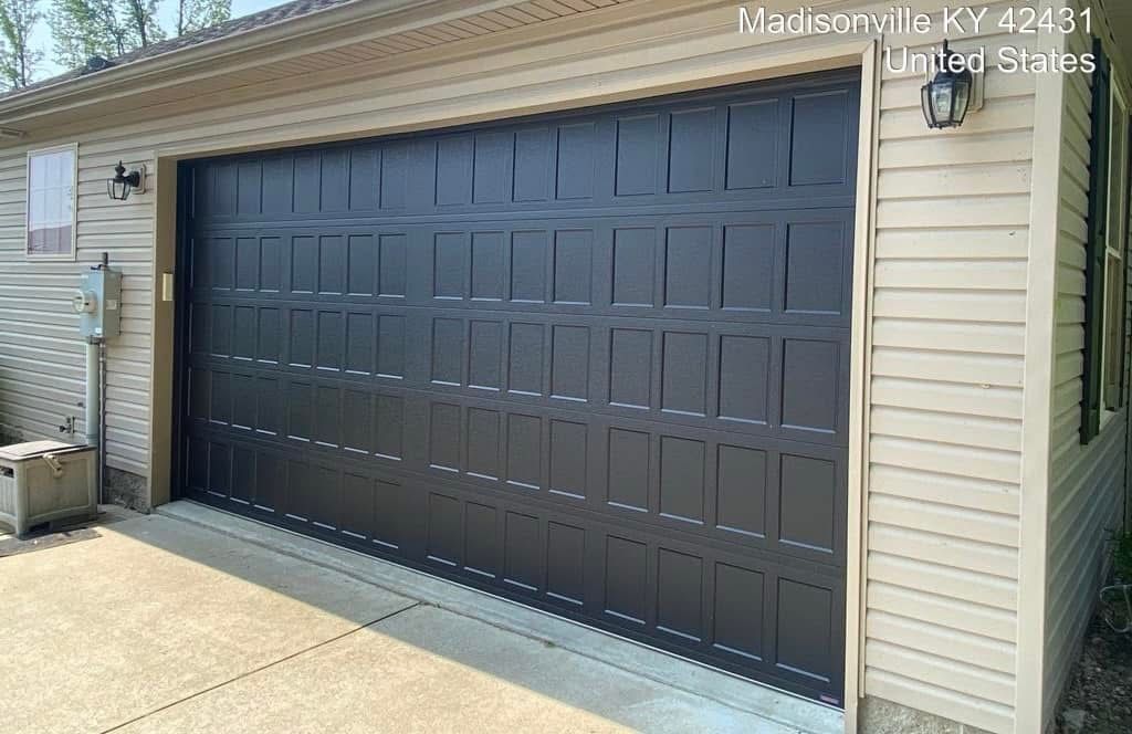 Black garage door with grid design, tan siding, and a lamp in Madisonville, KY.