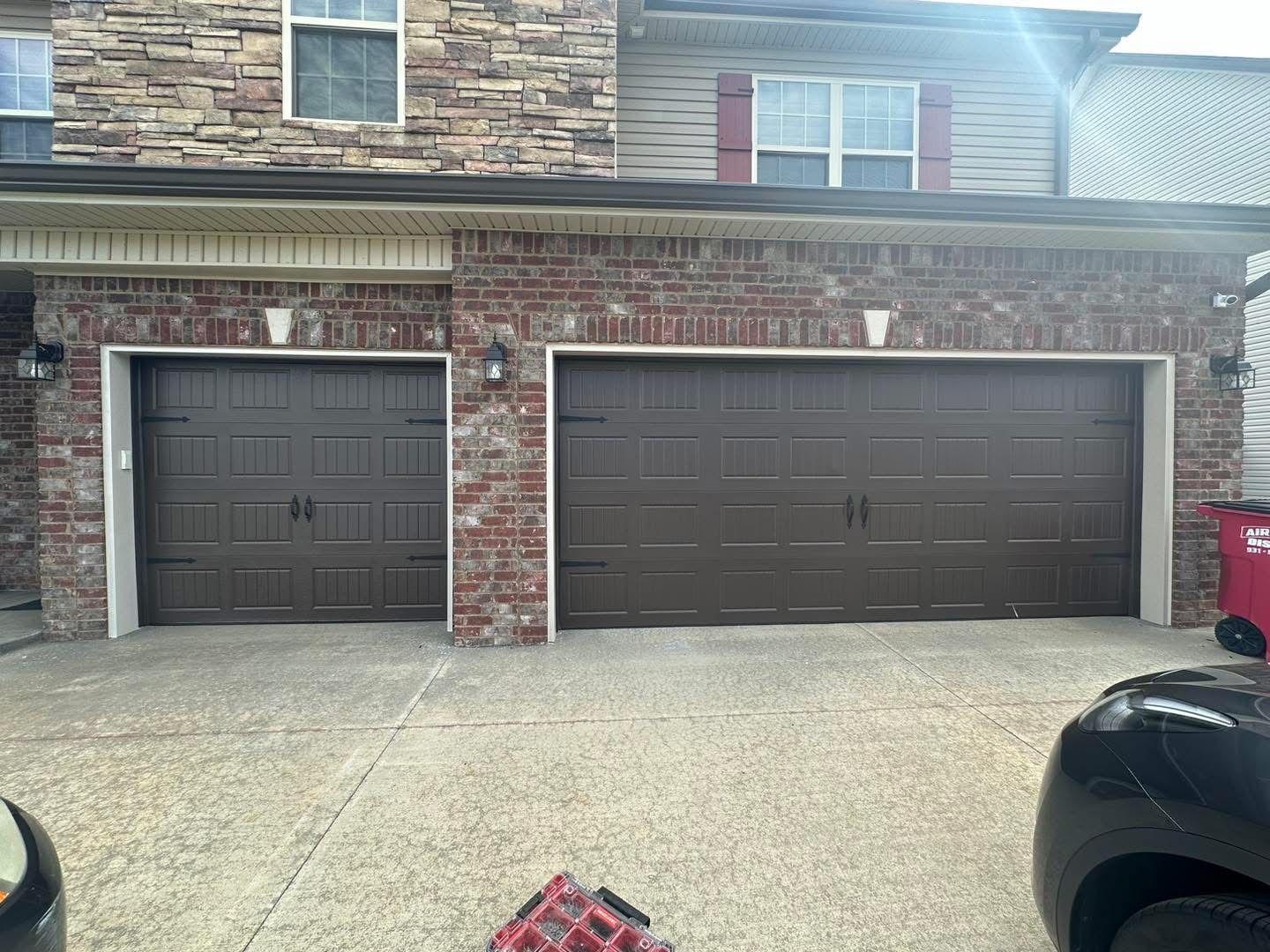 Two brown garage doors, one single and one double, on a brick and stone building.