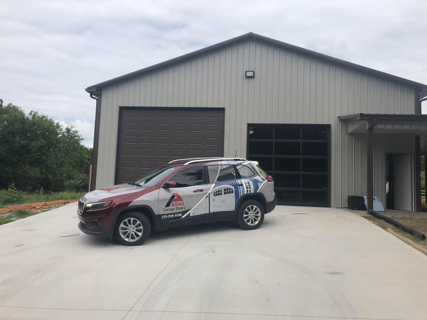 Red and white Jeep parked in front of a light gray building with large glass windows and a closed garage door.