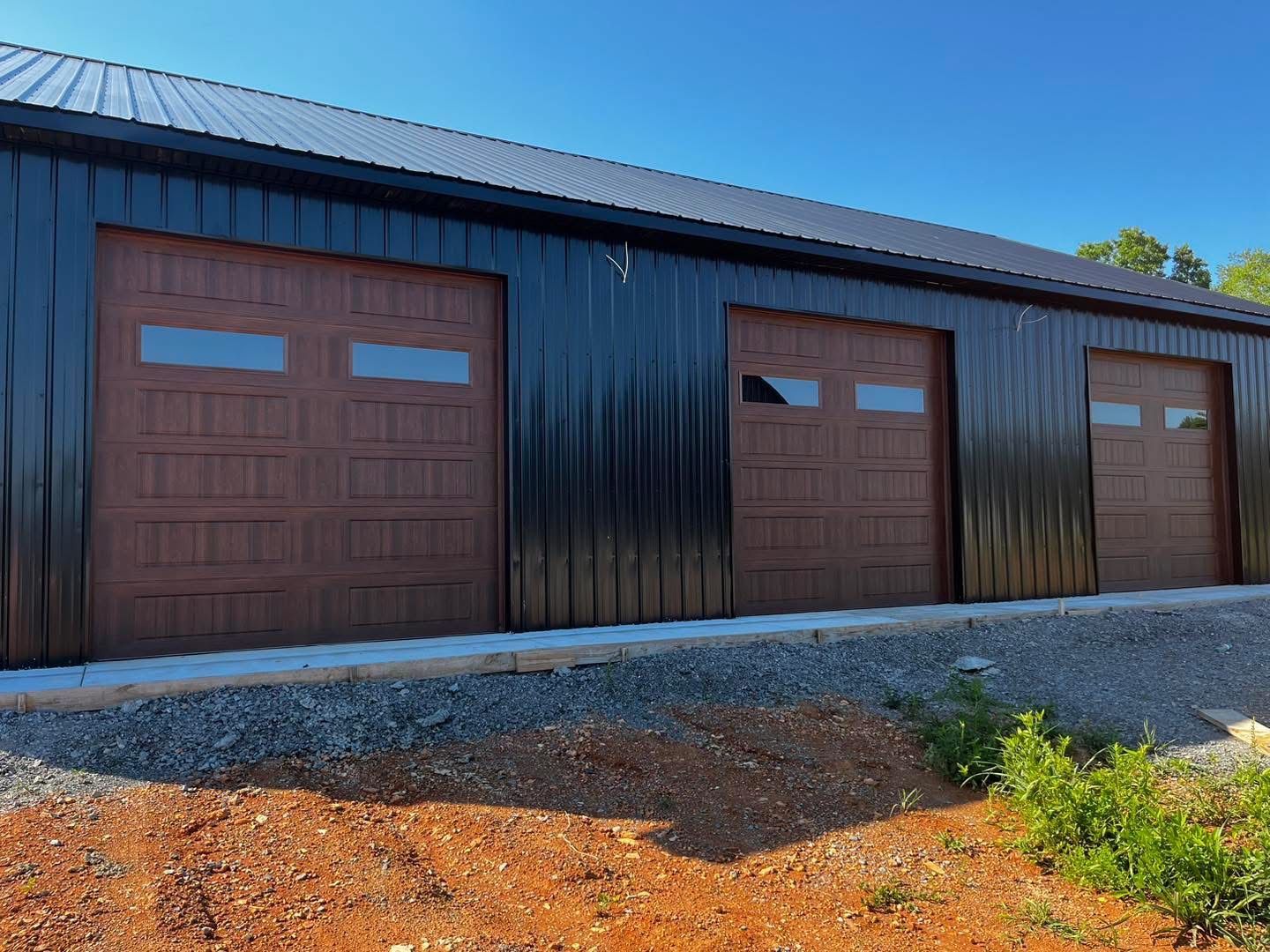 Three-bay garage with brown doors and windows in a black metal building under a bright blue sky.