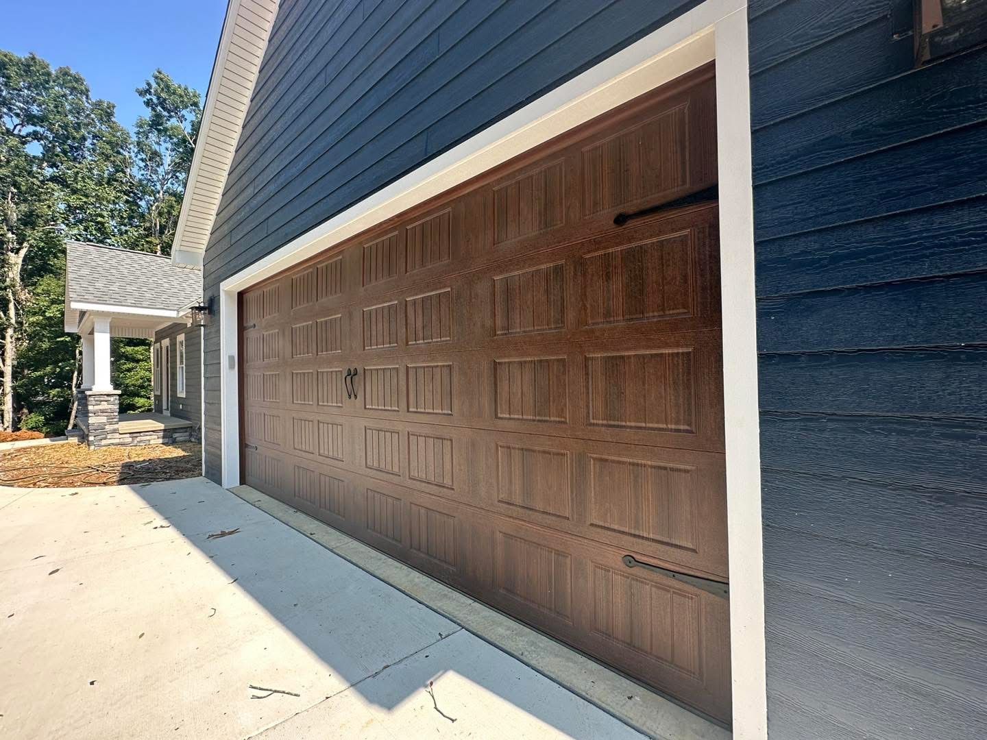 Brown garage door on a home with dark blue siding, concrete driveway, and white trim.