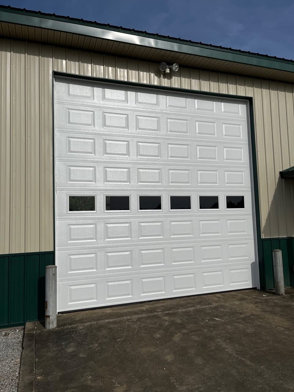 White garage door with windows on a tan and green building under a blue sky.