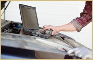 A person is using a laptop computer under the hood of a car