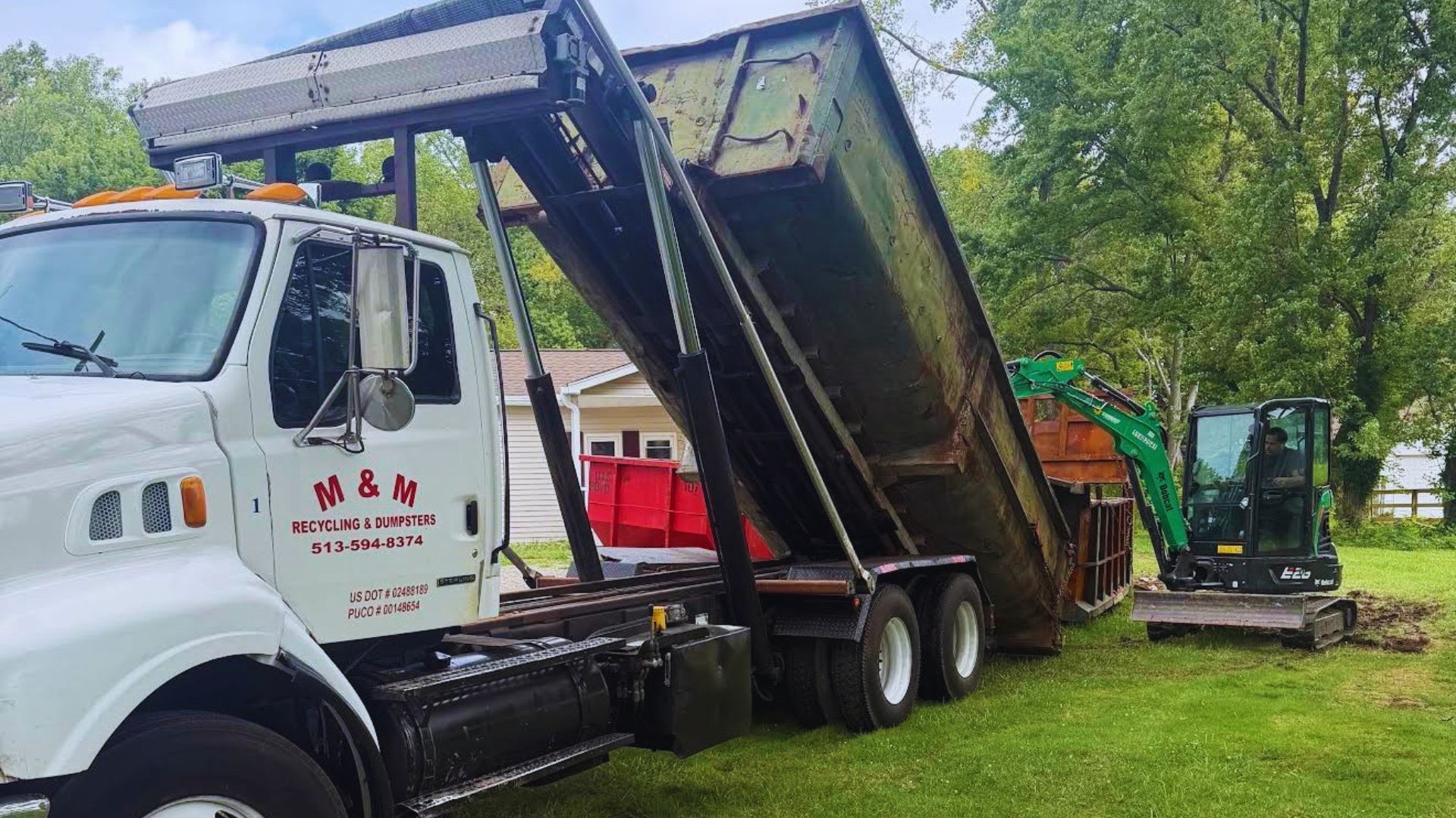 White dump truck tipping a raised trailer bed to unload dirt on a grassy construction site