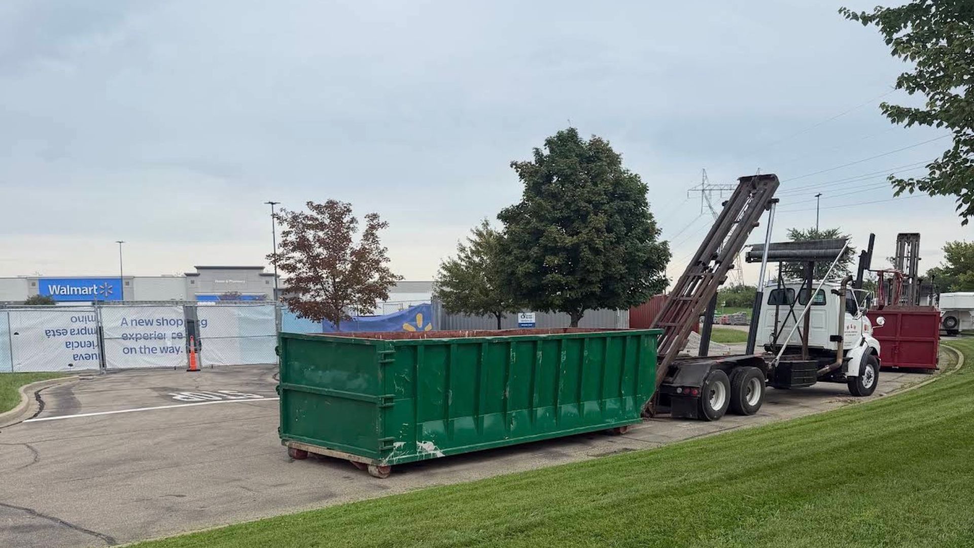 Construction dumpster being loaded onto a truck with a crane in a parking lot