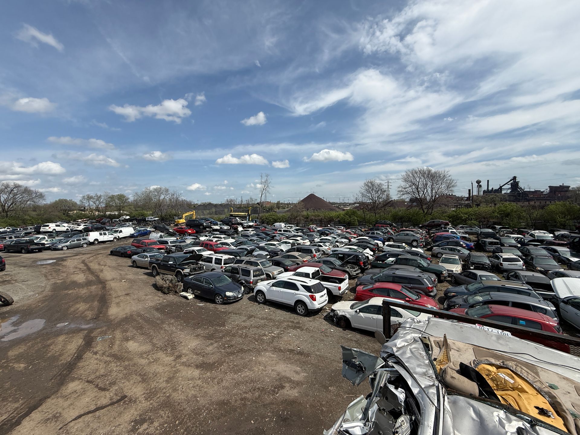 A sprawling junkyard filled with many wrecked cars under a sunny blue sky with thin clouds.