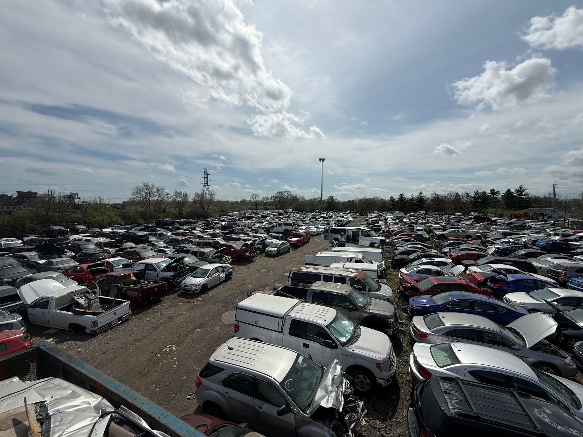 A high-angle view of a vast, crowded automotive salvage yard under a bright, cloudy sky.