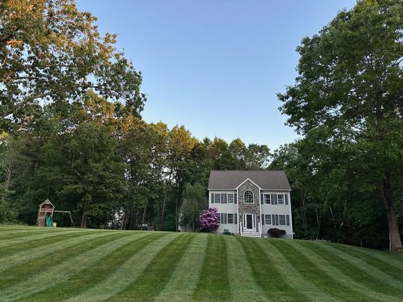 House on a striped green lawn with trees and a clear blue sky