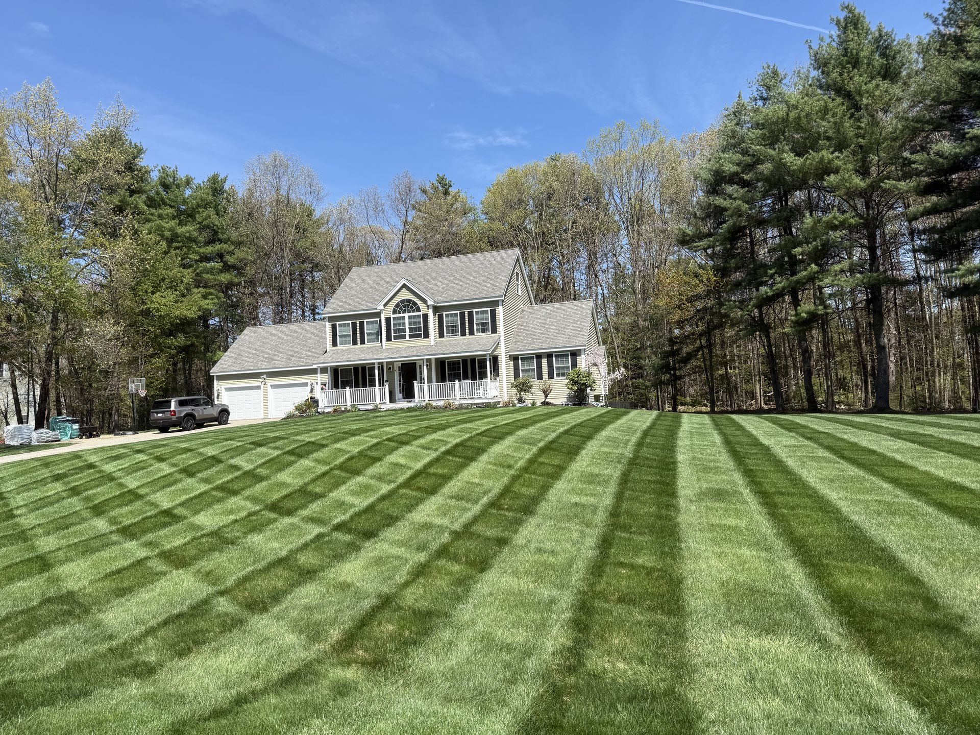 Two-story house with a striped green lawn, trees, and a blue sky on a sunny day