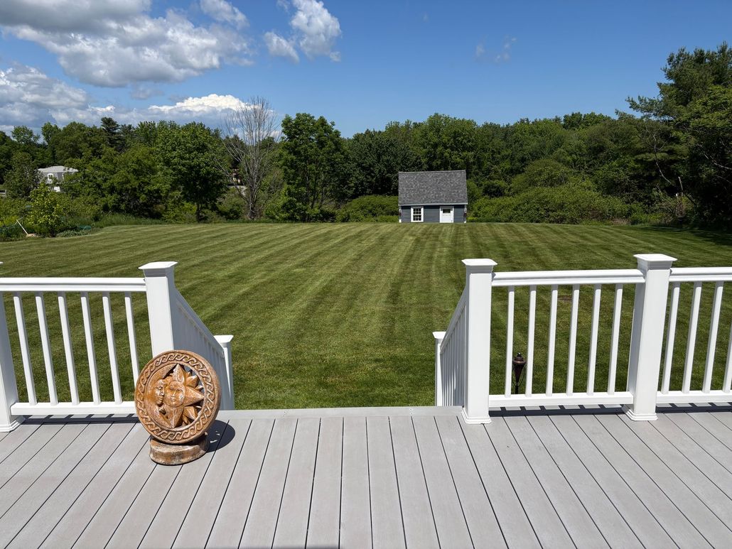 White deck overlooking a green lawn with a small shed and blue sky on a sunny day
