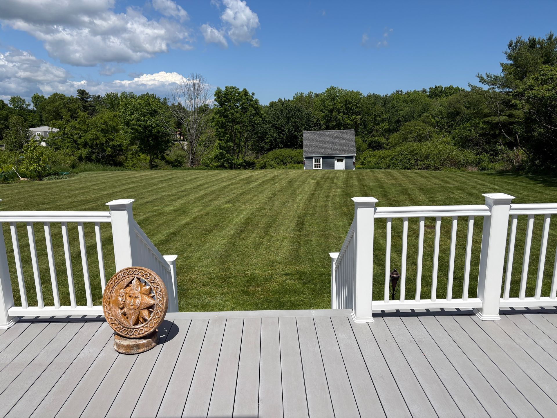 White deck overlooking a green lawn with a small shed and blue sky on a sunny day
