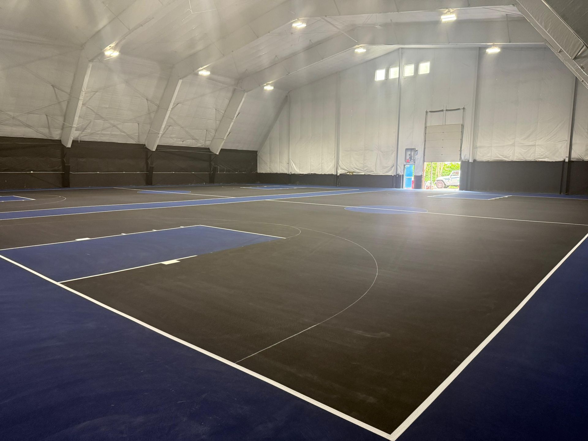 Indoor basketball court with black and blue floor, white lines, and bright lights.