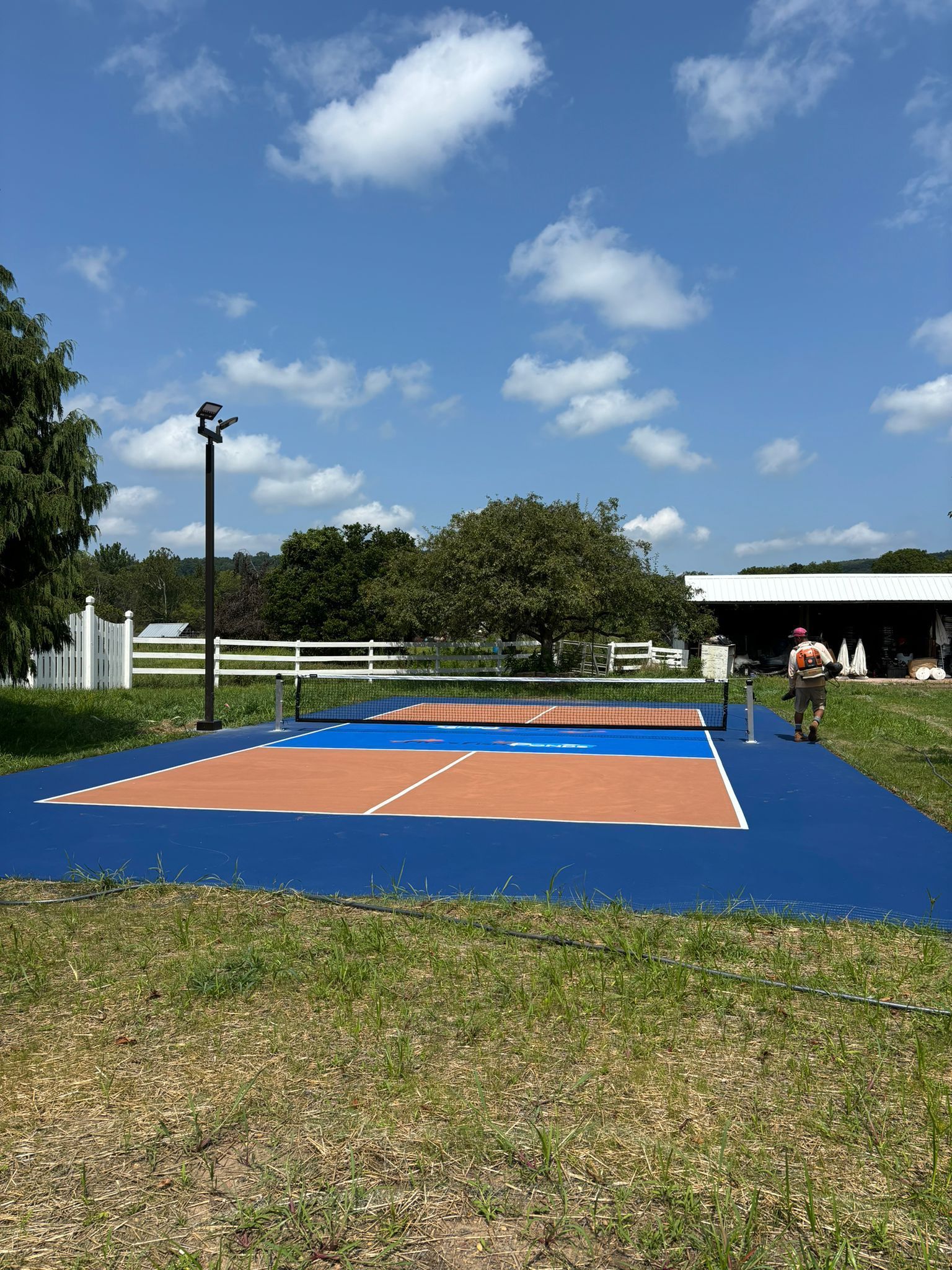 Outdoor volleyball court, blue and brown with a player, under a bright blue sky.