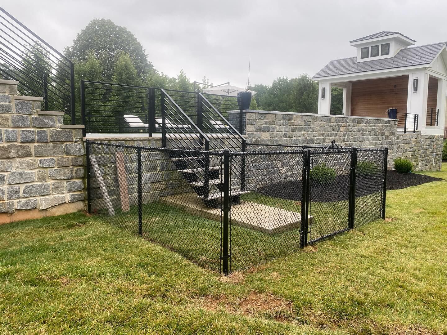 A black chain link fence surrounds a staircase in a backyard.