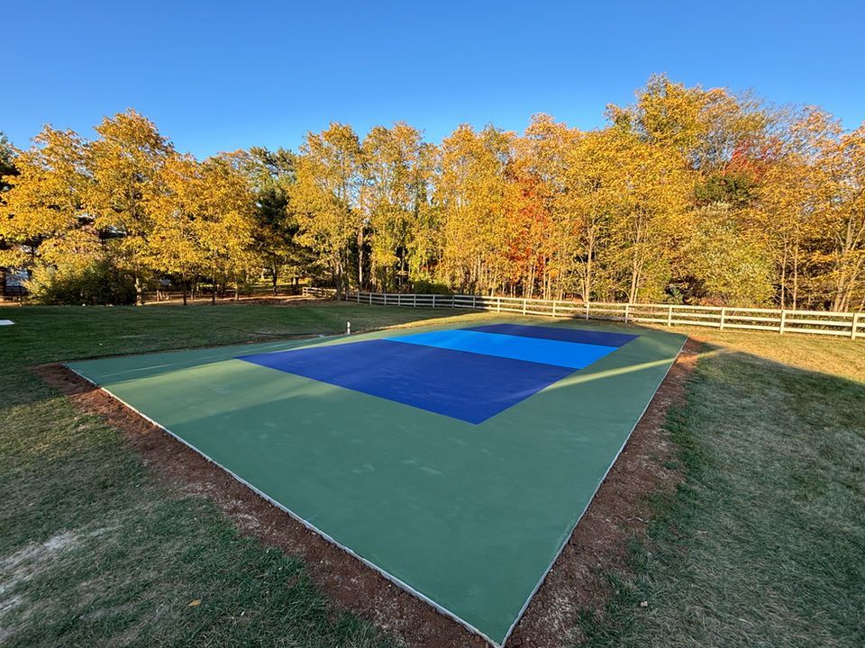 A basketball court in the middle of a field with trees in the background.