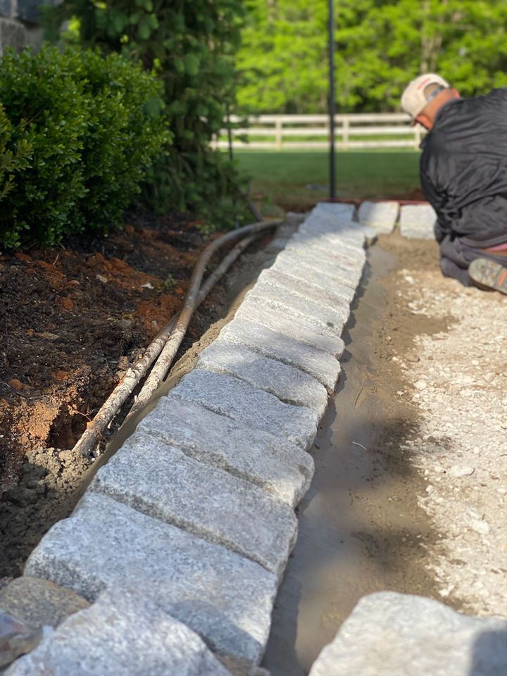 A man is laying a stone wall in a garden.