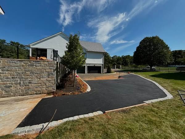 A driveway leading to a house with a stone wall and a garage.