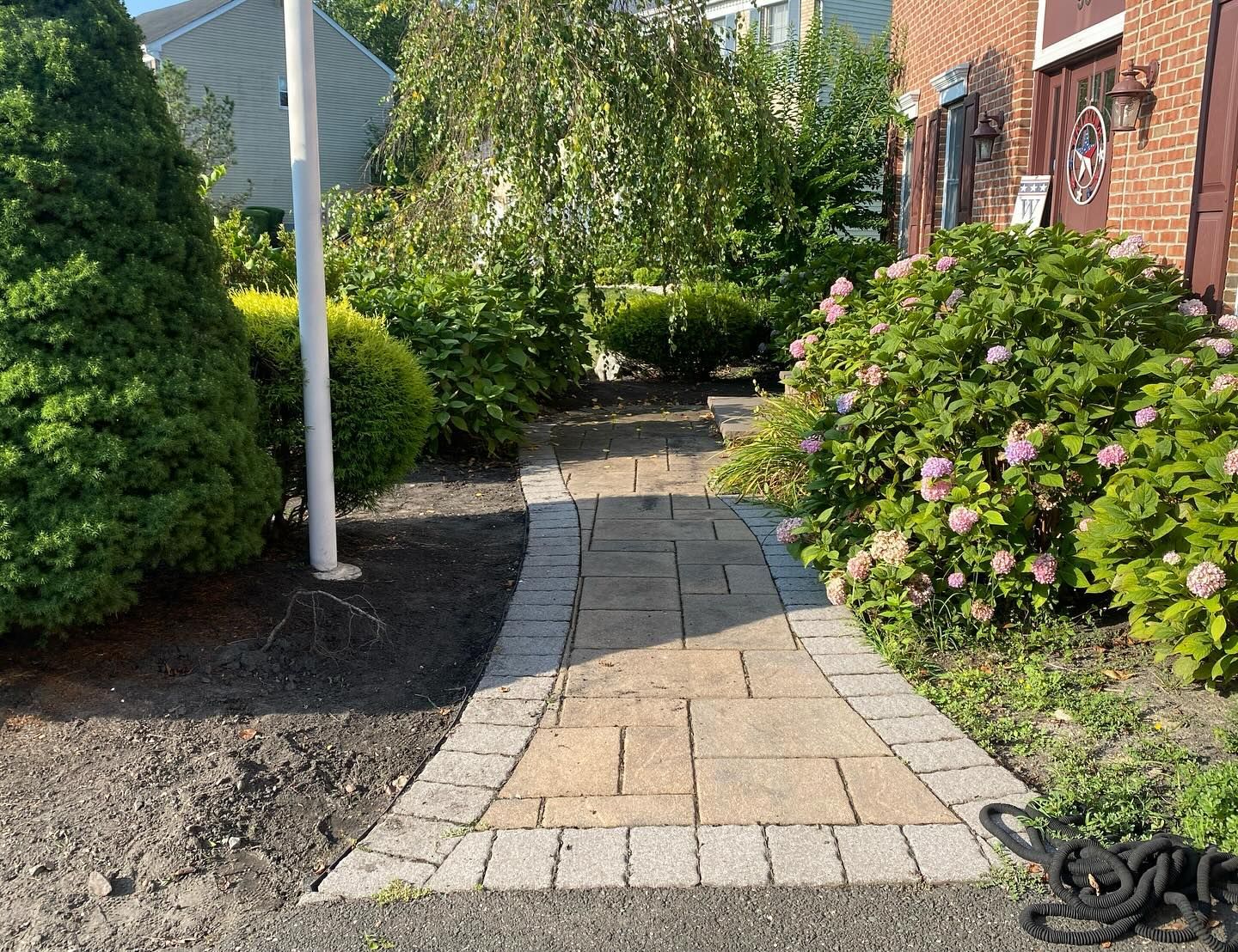 A brick walkway leading to a house with a flag pole in the background.
