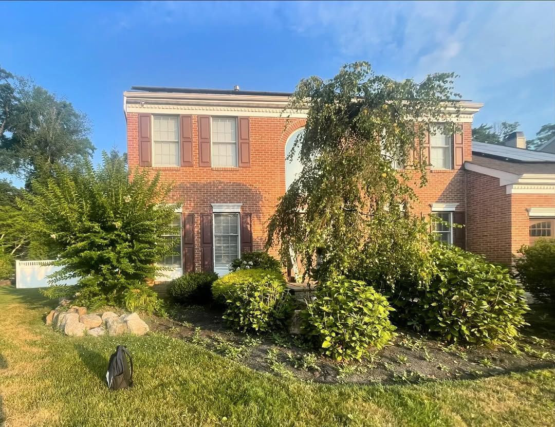 A large brick house with a lot of bushes and trees in front of it.