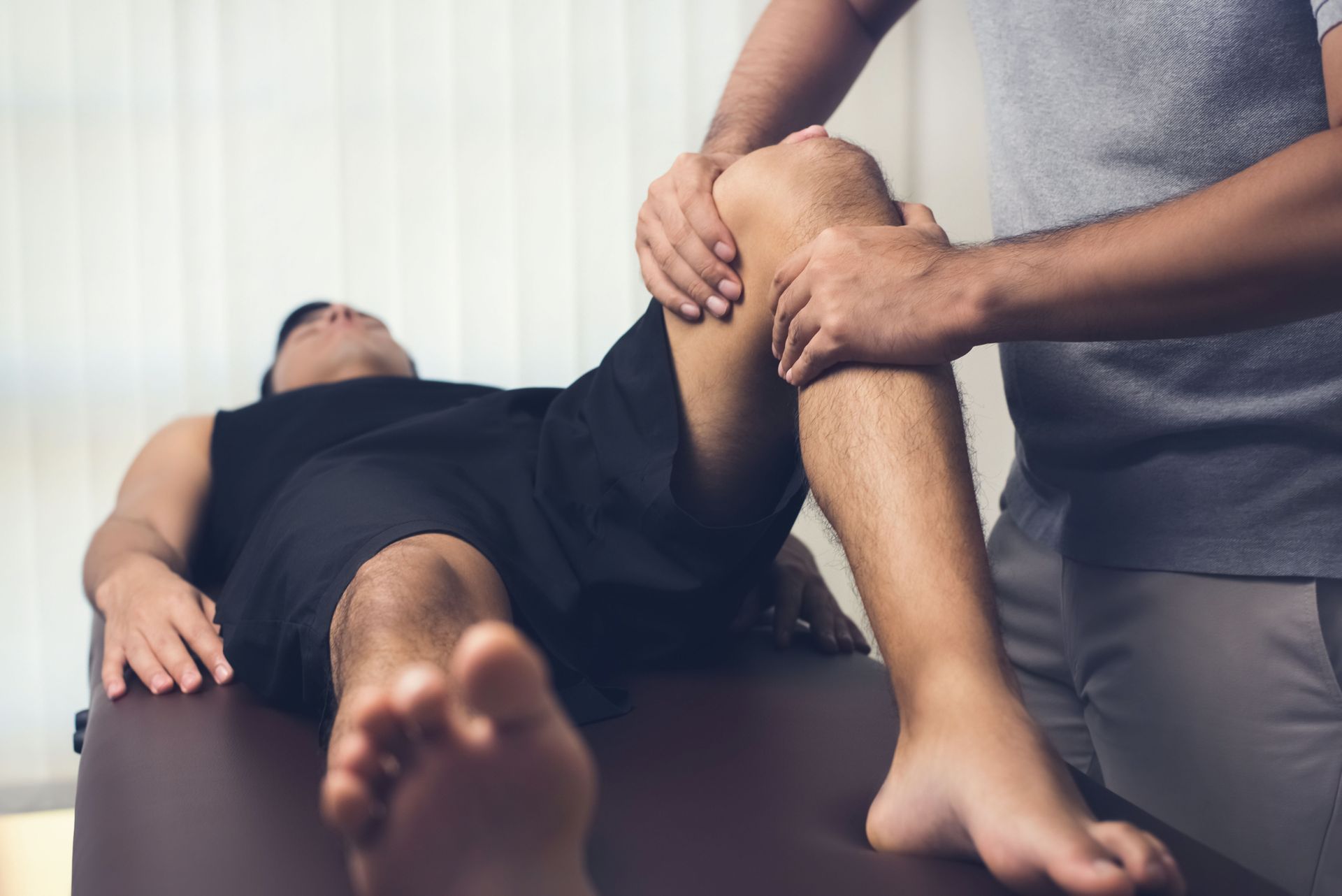 Man receiving knee treatment from a therapist, lying on a massage table.