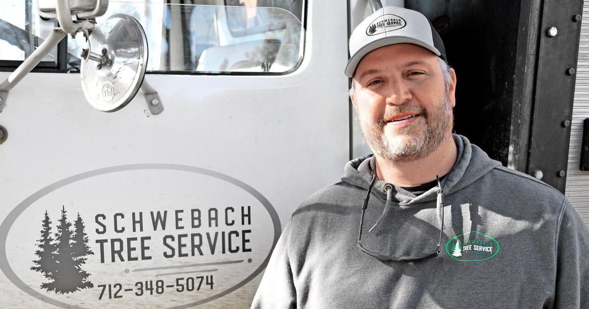 Man in front of a truck with "Schweback Tree Service" logo on the side. Gray hoodie, cap, mask.