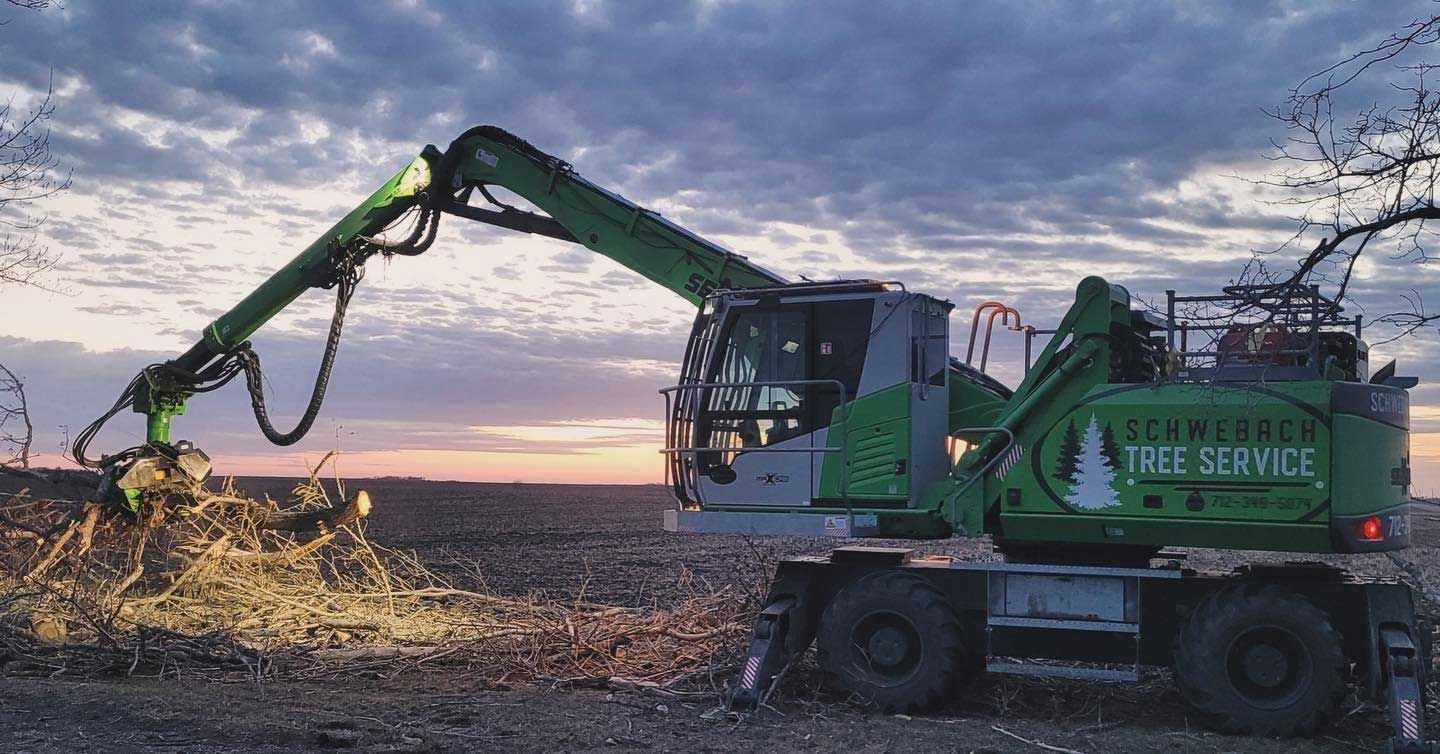 Green tree service machine cutting branches in a field at sunset.