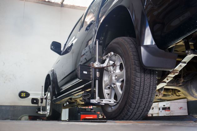 Black SUV on a wheel alignment lift in an auto repair shop