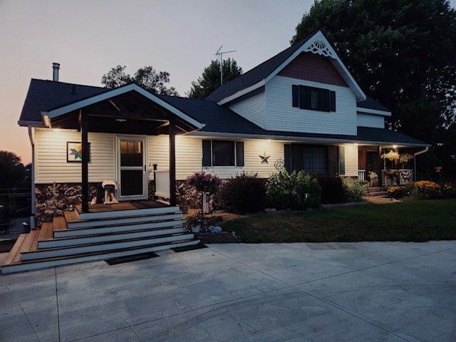 Two-story white house with dark roof and porch at dusk. Stone accents, lit up exterior, and a wide driveway.